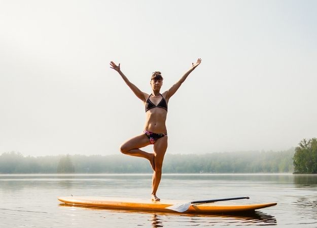 Mujer practicando yoga encima de tabla de paddle surf